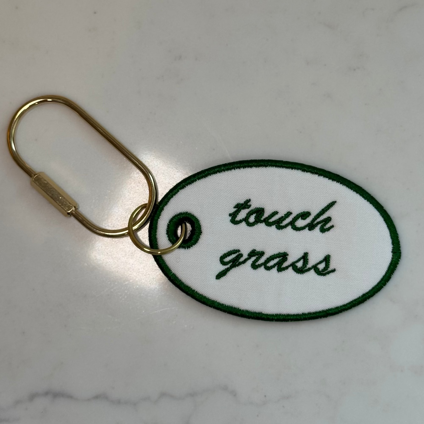 Keychain with 'touch grass' text on a marble surface